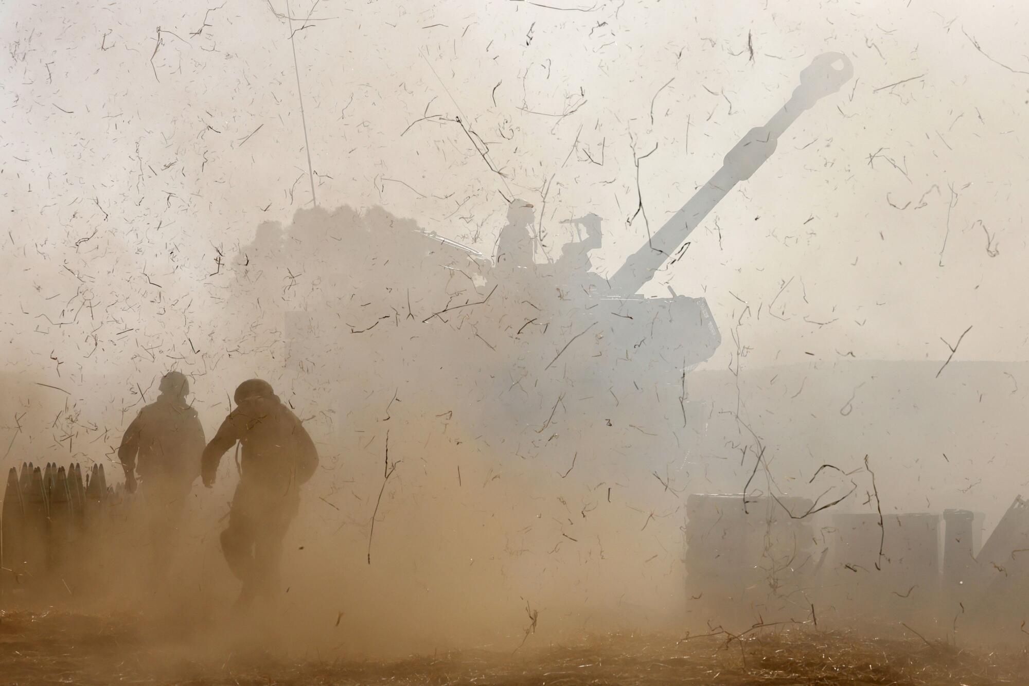 Israeli soldiers fire a howitzer amid smoke and flying debris