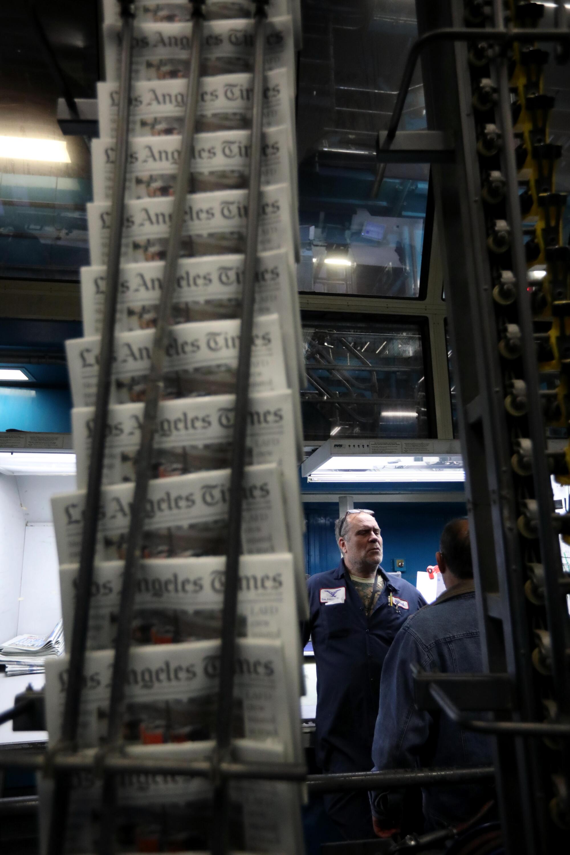 First color pressman Daniel Koval stands near a conveyor belt that transports Times newspapers.