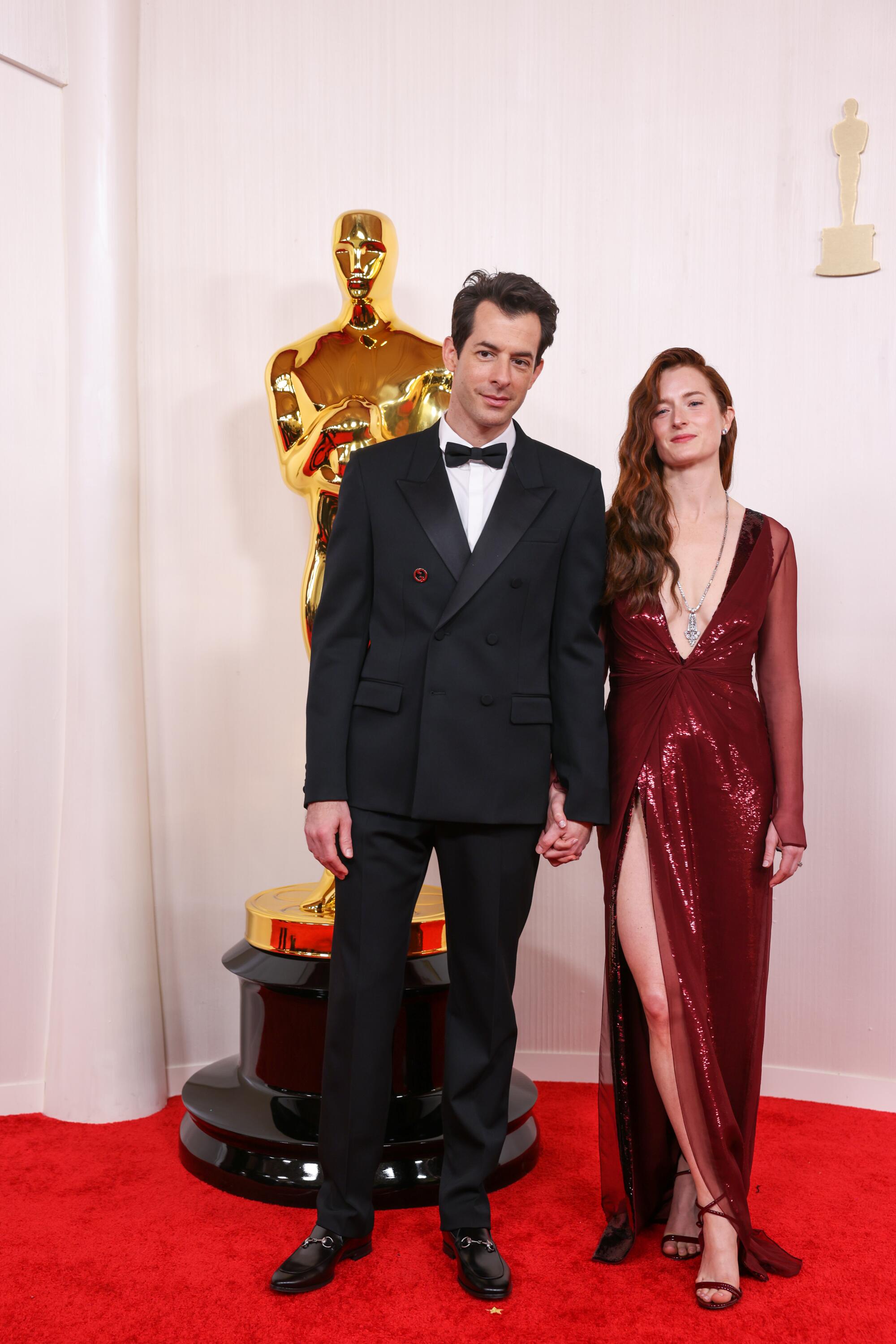 Mark Ronson, in a black suit, and Grace Gummer, in a red dress with a high leg slit, pose for cameras. 