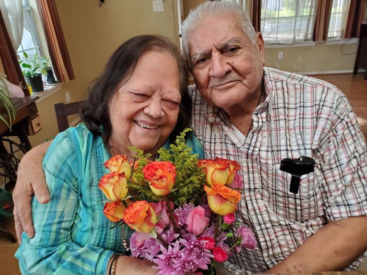 Licha, who is holding flowers, and Felipe Castillo pose for the camera and smile.