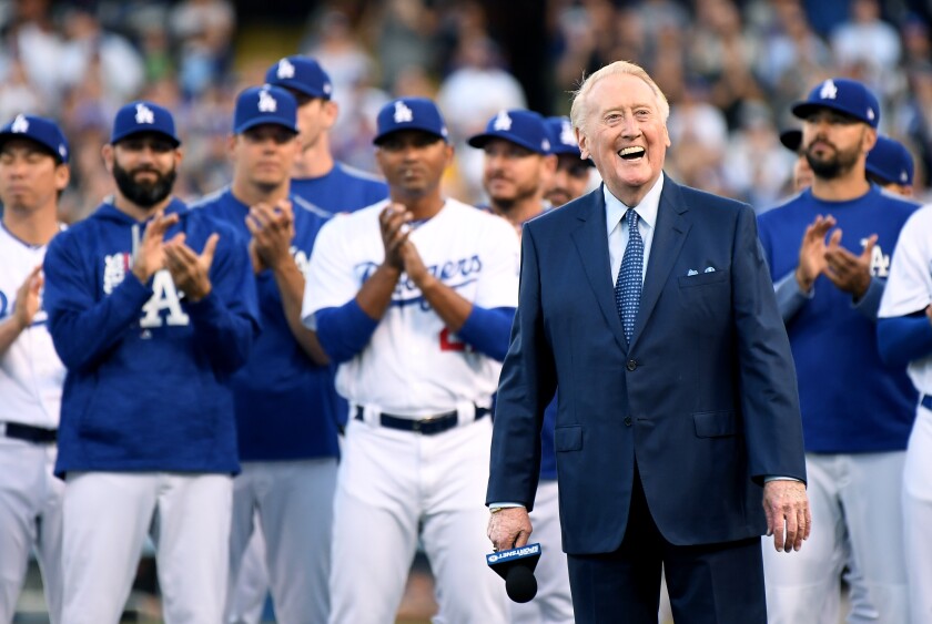 Vin Scully smiles as he is inducted into the Dodgers' ring of honor as players clap behind him.