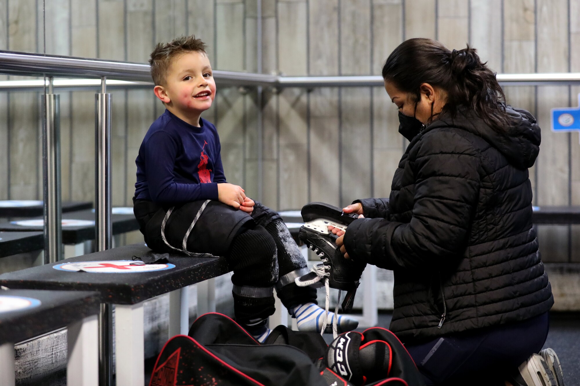 A player in the Mexico City Jr. Kings youth hockey program gets help with removing his skates after practicing.