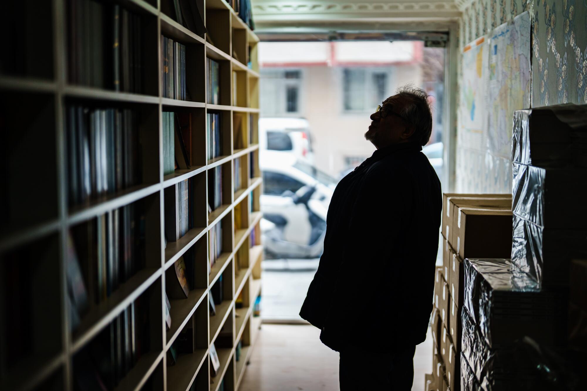 A man shown in silhouette looks up at books on shelves 