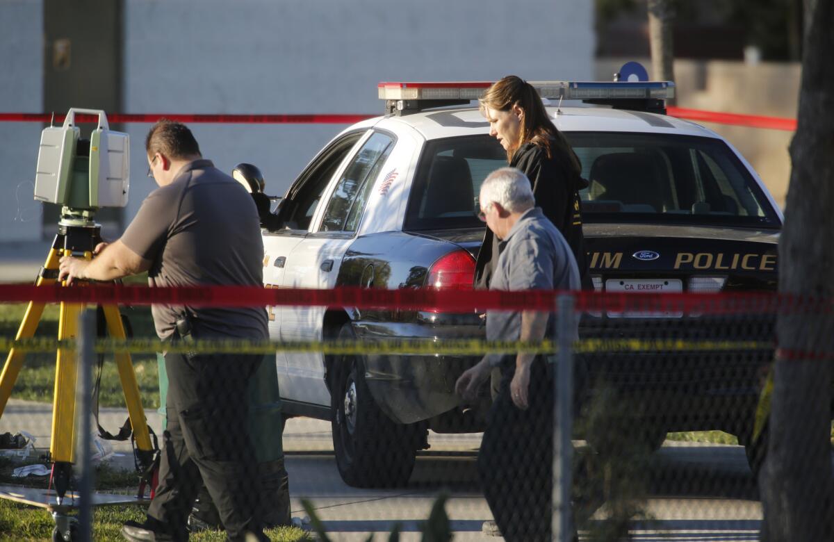 Investigators pass by the patrol car where an Anaheim police pfficer shot and killed a 22-year-old man in Sage Park in Anaheim on Feb. 9.