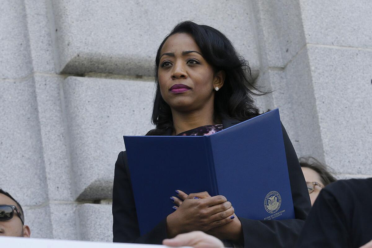 A woman holding a folder looks on as other people speak during a news conference.