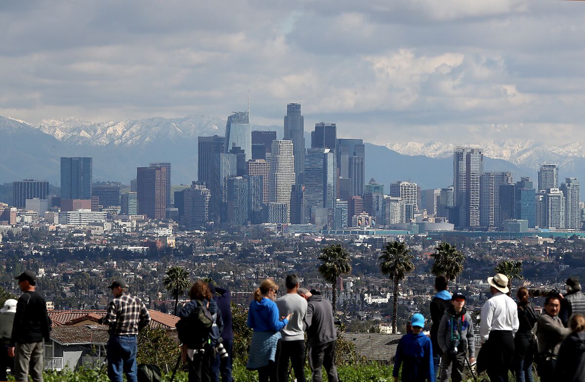 People gather for a look at snowcapped mountains in the distance, behind skyline buildings