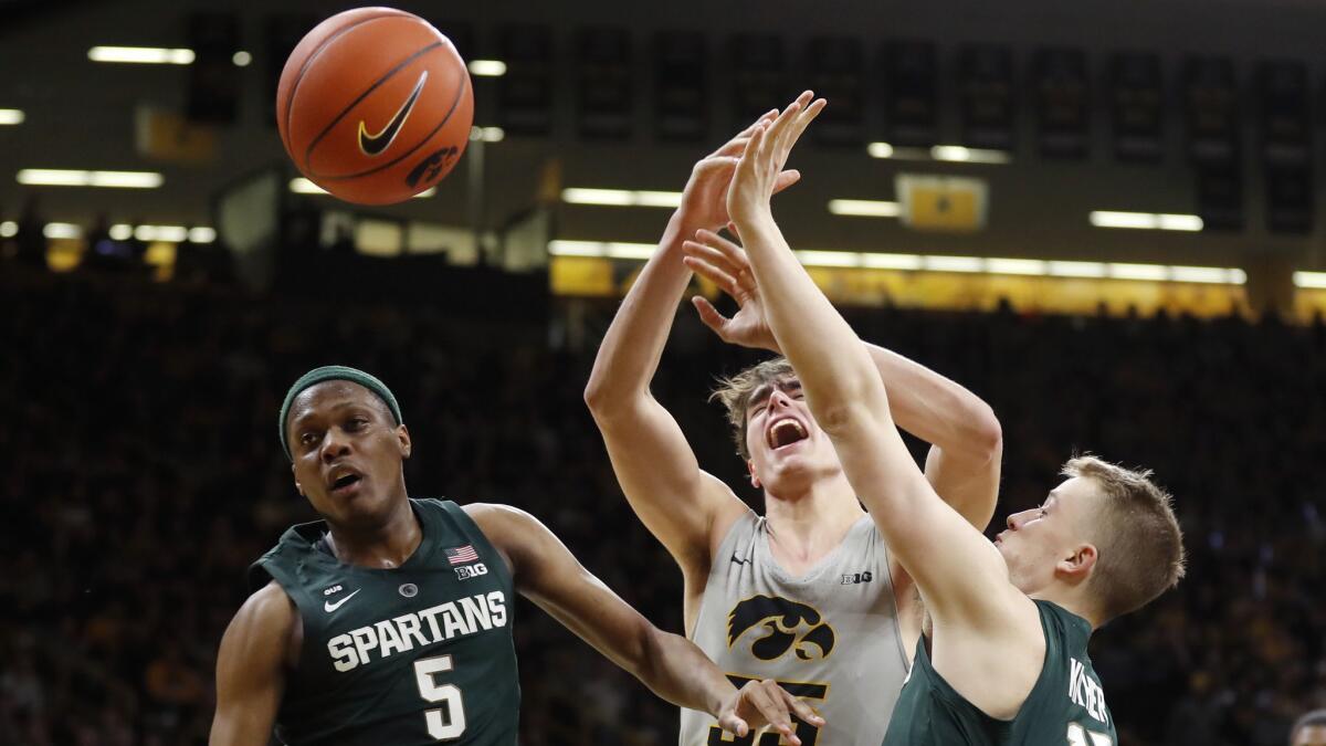 Iowa forward Luka Garza, center, fights for a rebound with Michigan State's Cassius Winston, left, and Thomas Kithier during the second half.