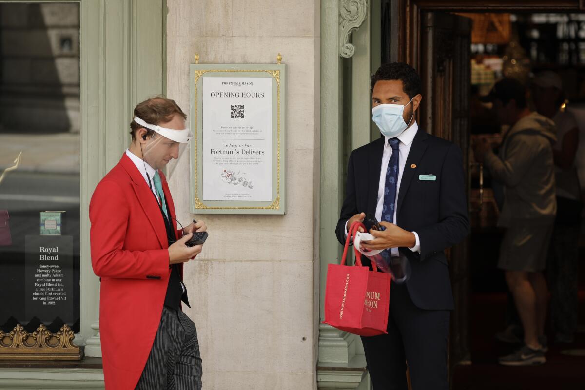 A doorman and colleague stand at the main entrance of the Fortnum & Mason department store in London. Parts of the store have reopened to customers.