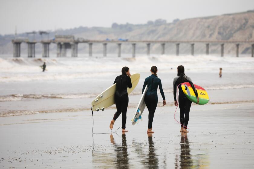 Surfers Ava Moylan, left, Brooke Norris, and Allison Gall walk to the water at La Jolla Shores beach on April 30, 2020. Gov. Gavin Newsom announced that San Diego County beaches would be allowed to remain open.