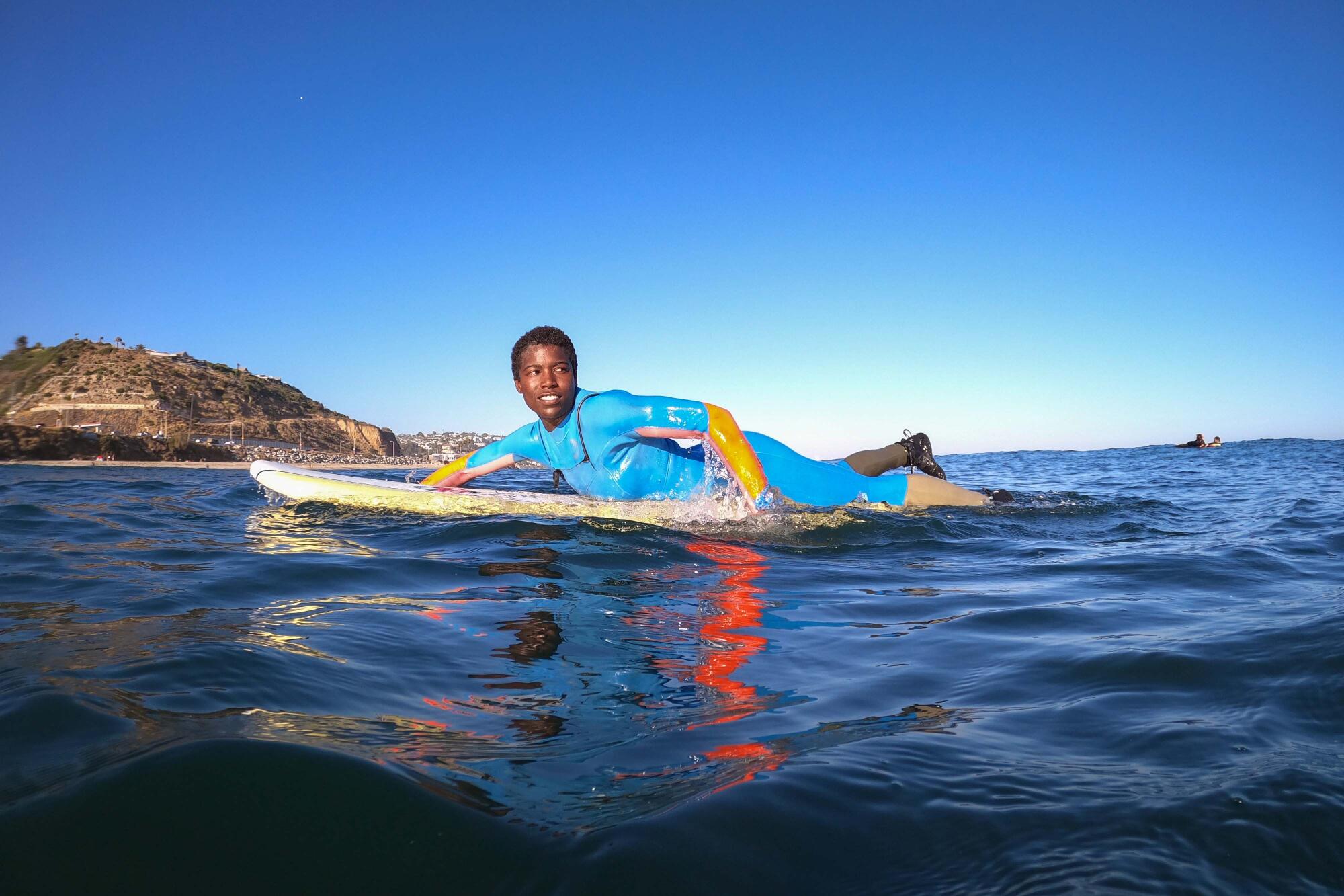 A person lying down on a surfboard and paddling in the ocean