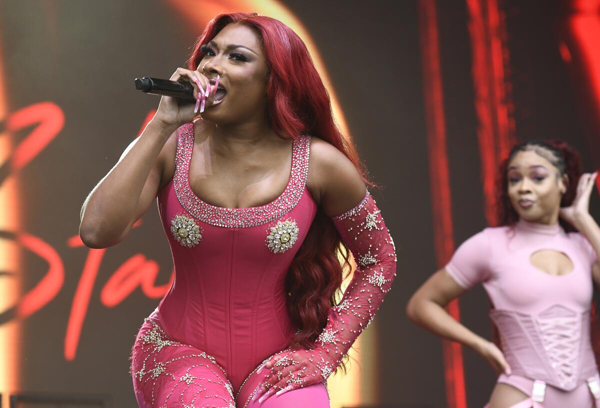 Megan Thee Stallion raps into a microphone on stage in a pink jumpsuit with silver accents
