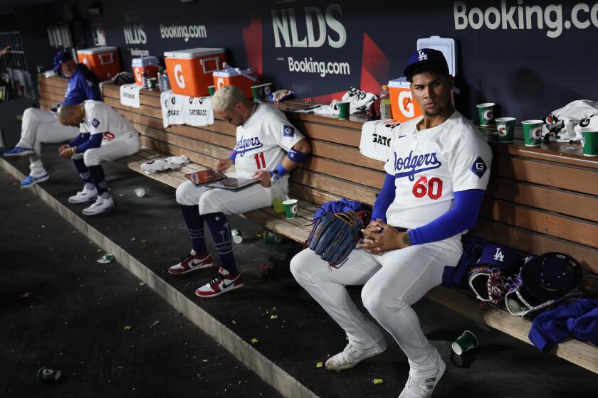 LOS ANGELES, CALIFORNIA - OCTOBER 06: Edgardo Henriquez #60 of the Los Angeles Dodgers sits with Miguel Rojas #11 and Mookie Betts #50 in the dugout during the ninth inning in game two of the National League Division Series against the San Diego Padres at Dodger Stadium on Sunday, Oct. 6, 2024 in Los Angeles. (Robert Gauthier / Los Angeles Times)