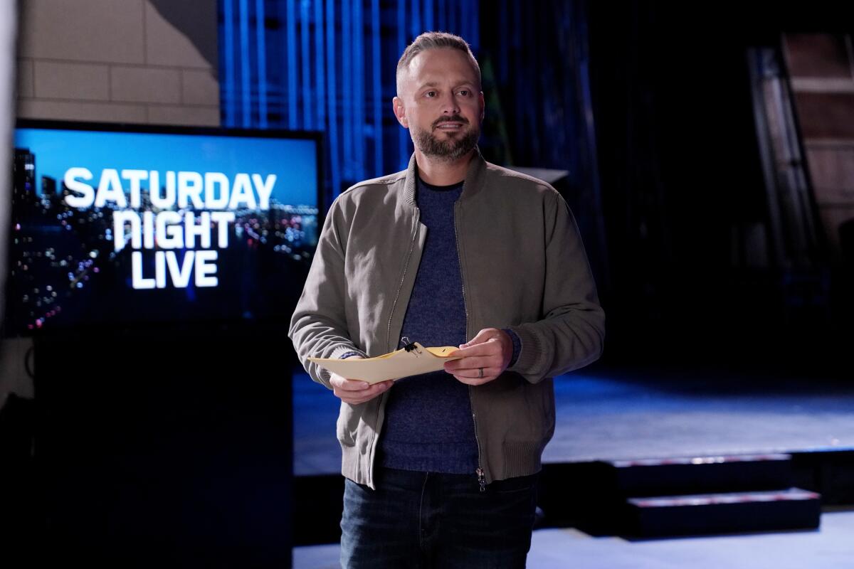 Nate Bargatze stands with note cards in his hands near a monitor that says Saturday Night Live.