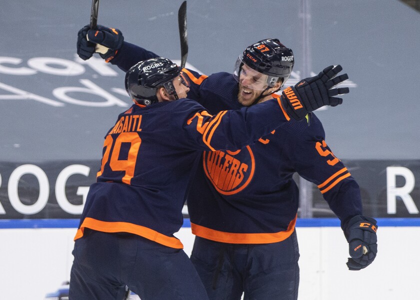 Edmonton Oilers' Connor McDavid (97) and Leon Draisaitl (29) celebrates after McDavid's 100th point of the season, during the second period of an NHL hockey game against the Vancouver Canucks on Saturday, May 8, 2021, in Edmonton, Alberta. (Jason Franson/The Canadian Press via AP)