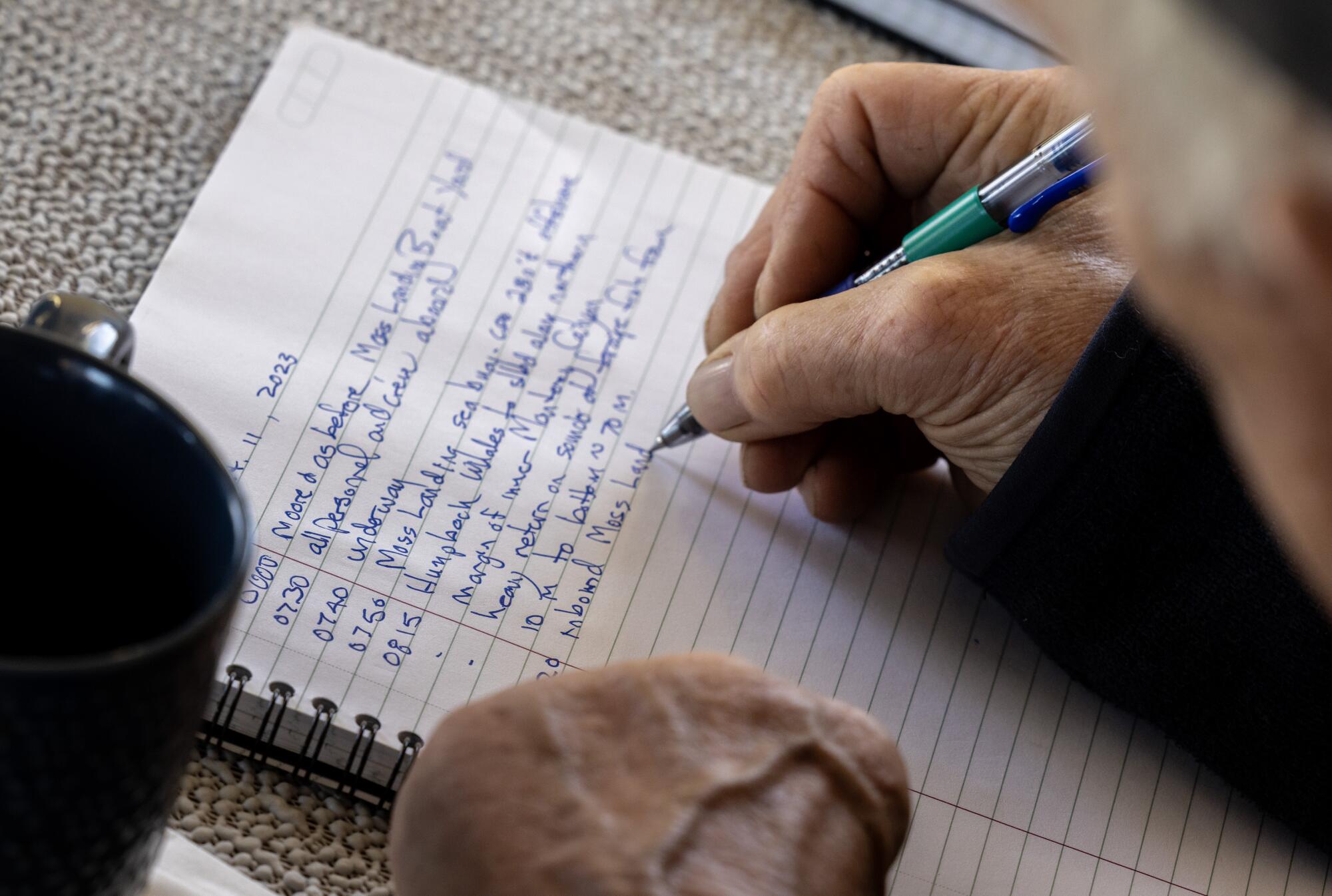 A close-up a man's hand writing on a notebook with a pen in blue ink.