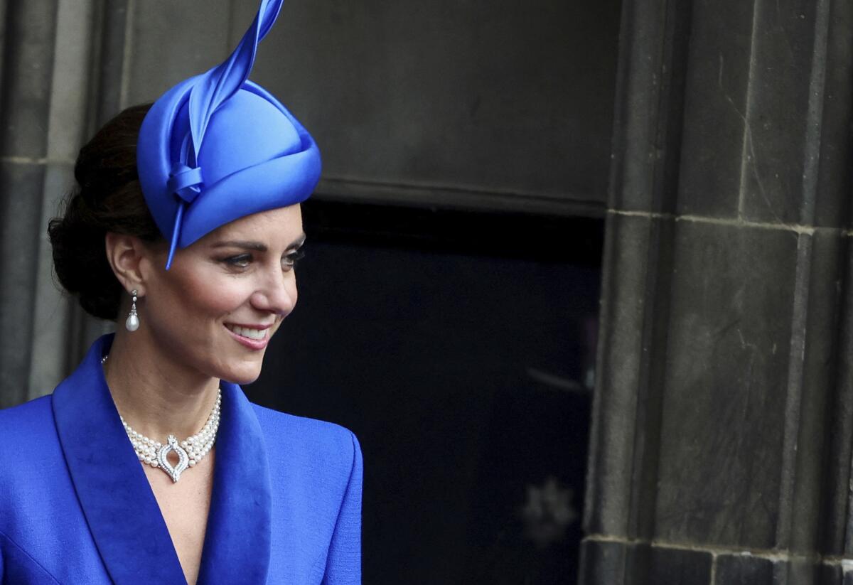 Kate Middleton wears a bright blue blazer and fascinator as she looks out in front of a large door