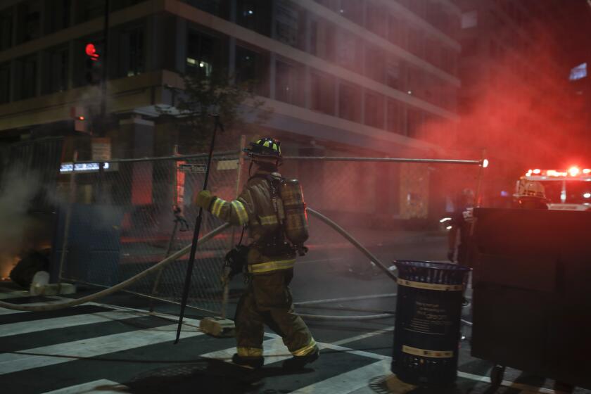 Firefighters put out a dumpster fire as protesters and police gather at Lafayette Park near the White House in Washington on Monday, June 22, 2020, after protesters tried to topple a statue of Andrew Jackson before being dispersed by police. (AP Photo/Maya Alleruzzo)