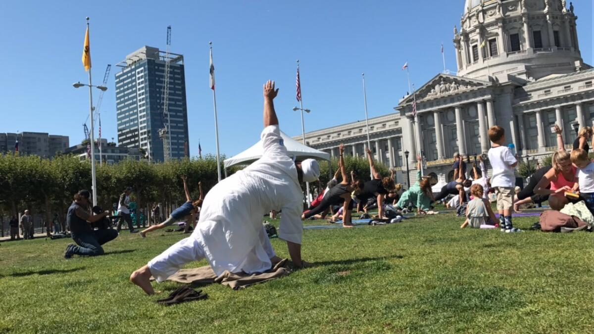 A group of yoga participates move through poses outside the Civic Center in San Francisco.