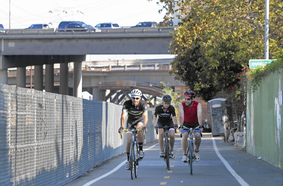 Bicyclists ride on a path along Egret Park in Los Angeles. In the background is the 5 Freeway.