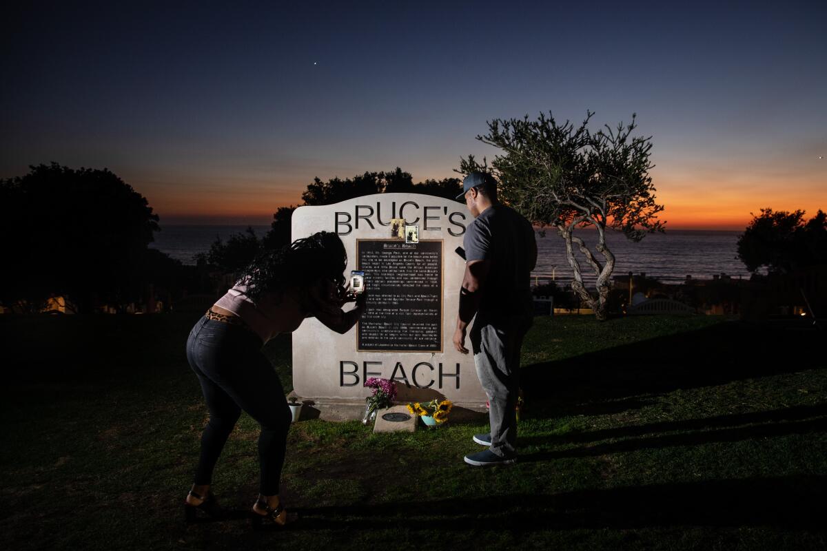 At twilight, two people visit a plaque at a beach park.