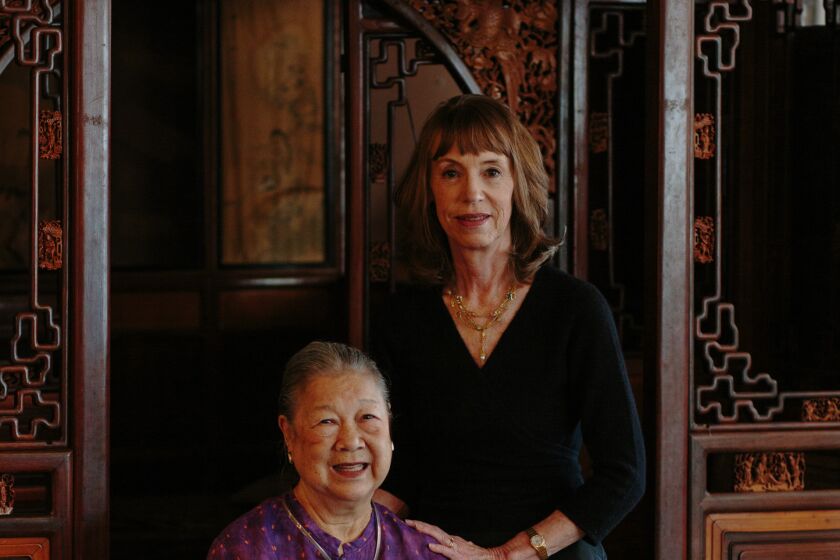 Two women, one seated and one standing, pose inside an antiques store.