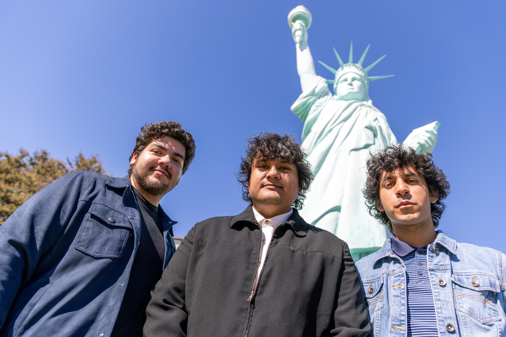 Three men pose in front of the Statue of Liberty replica in El Monte