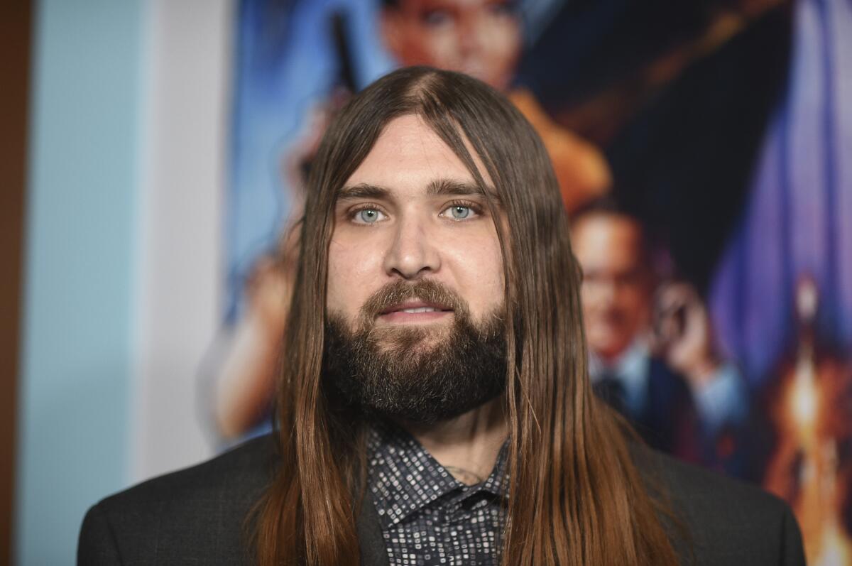 Weston Cage, who has long brown hair and a beard, posing at a movie premiere in a spotted shirt and black blazer