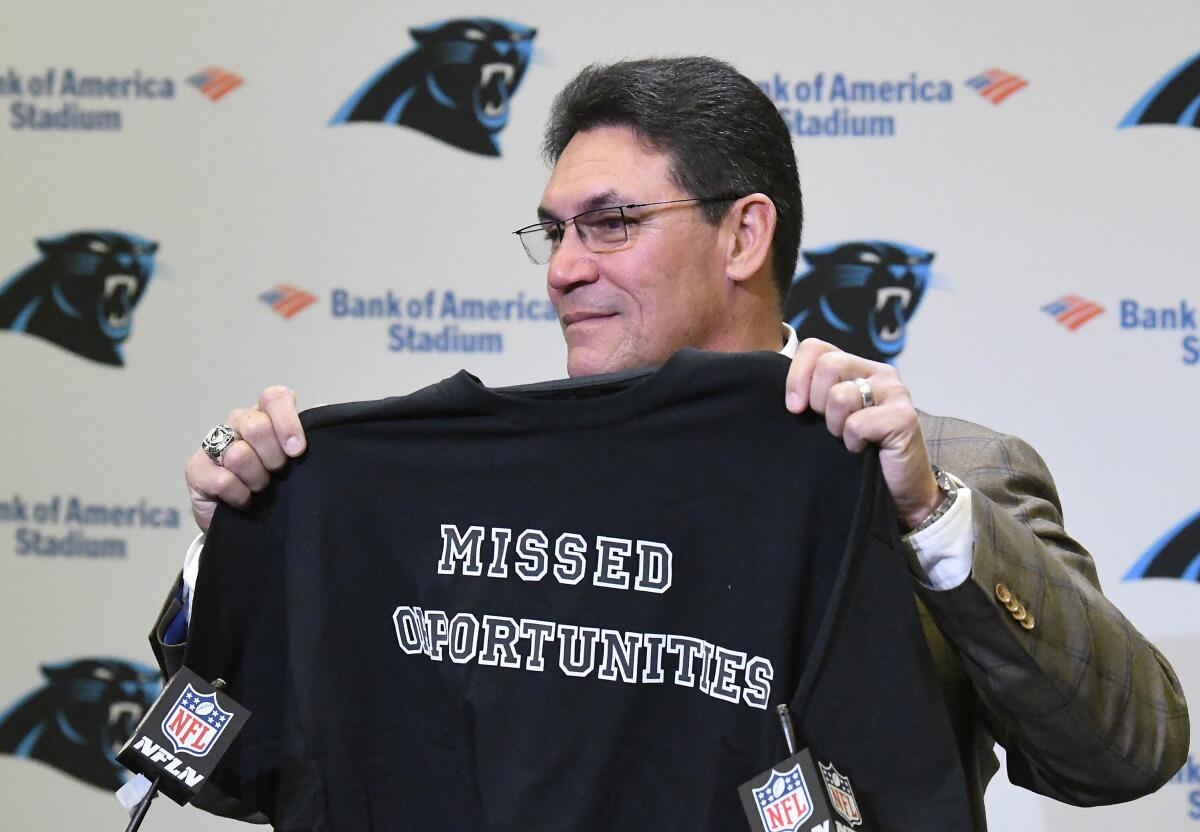 Former Carolina Panthers NFL football head coach Ron Rivera holds up a T-shirt at the end of a news conference.