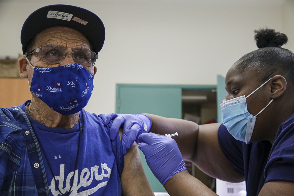 A nurse administers a shot to a man in a Los Angeles Dodgers T-shirt and mask