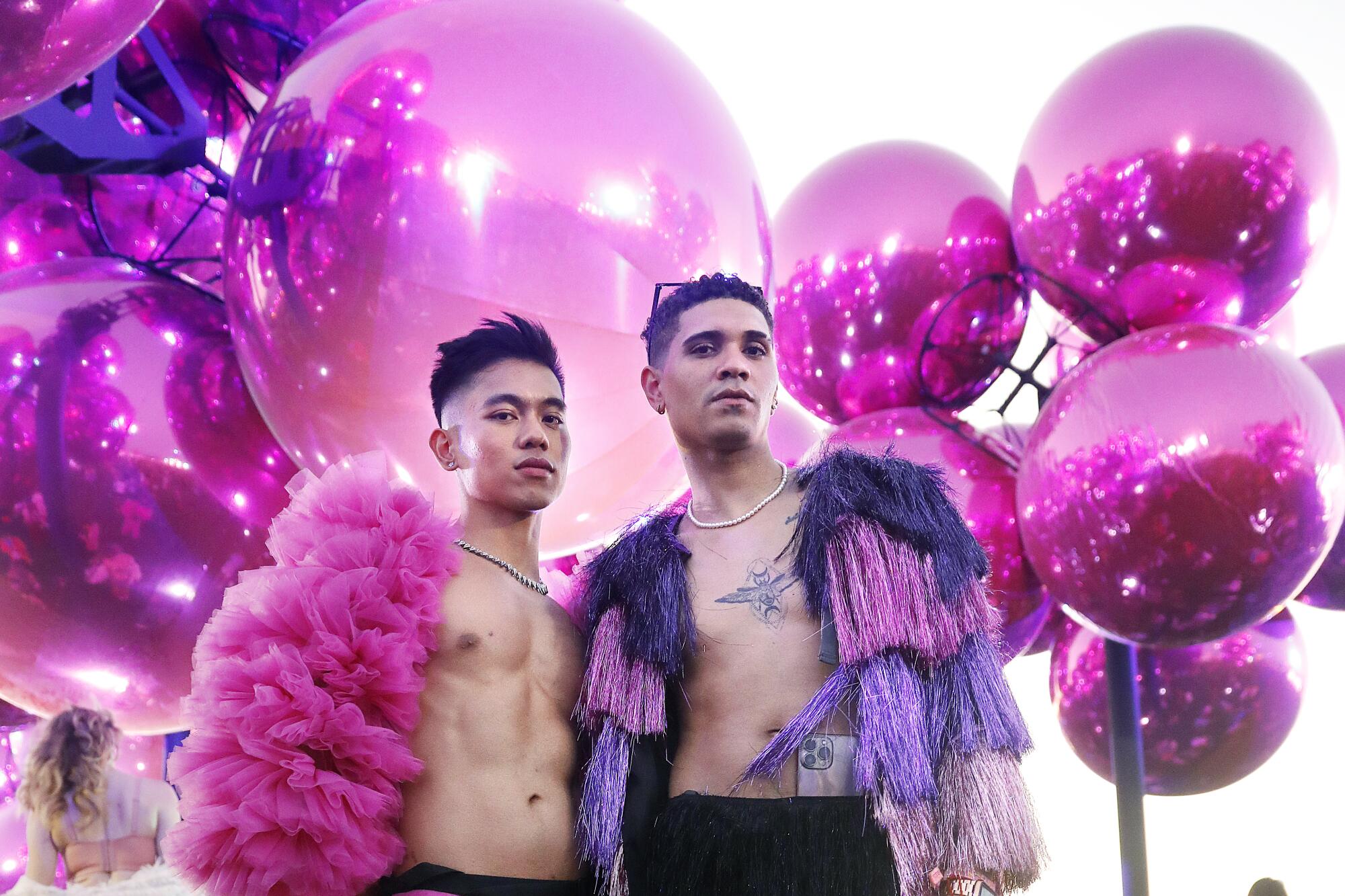 Two people pose for a fashion portrait in front of a sculpture of pink globes. 
