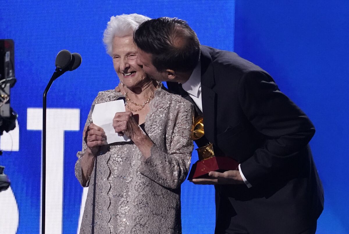 An elder woman gets a kiss on the cheek while accepting an award onstage