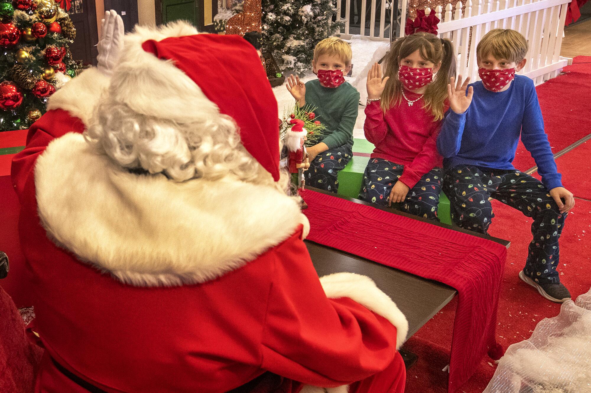 Griffin Hodge, 5, sister Delaney, 7, and brother Wyatt, 10, wear protective masks while sitting at a safe distance from Santa