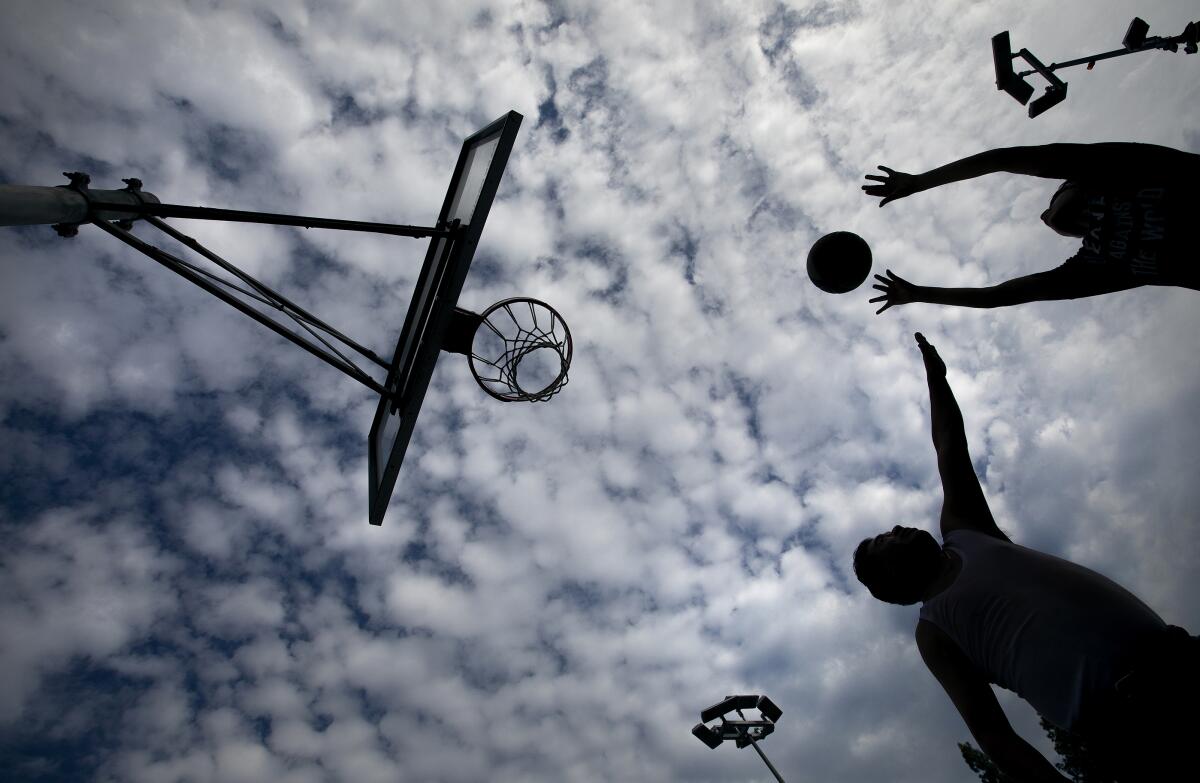 Seen from below, two people playing basketball are silhouetted against a partly cloudy sky