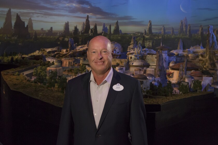 A man in a suit and tie in front of a picture of an animated town