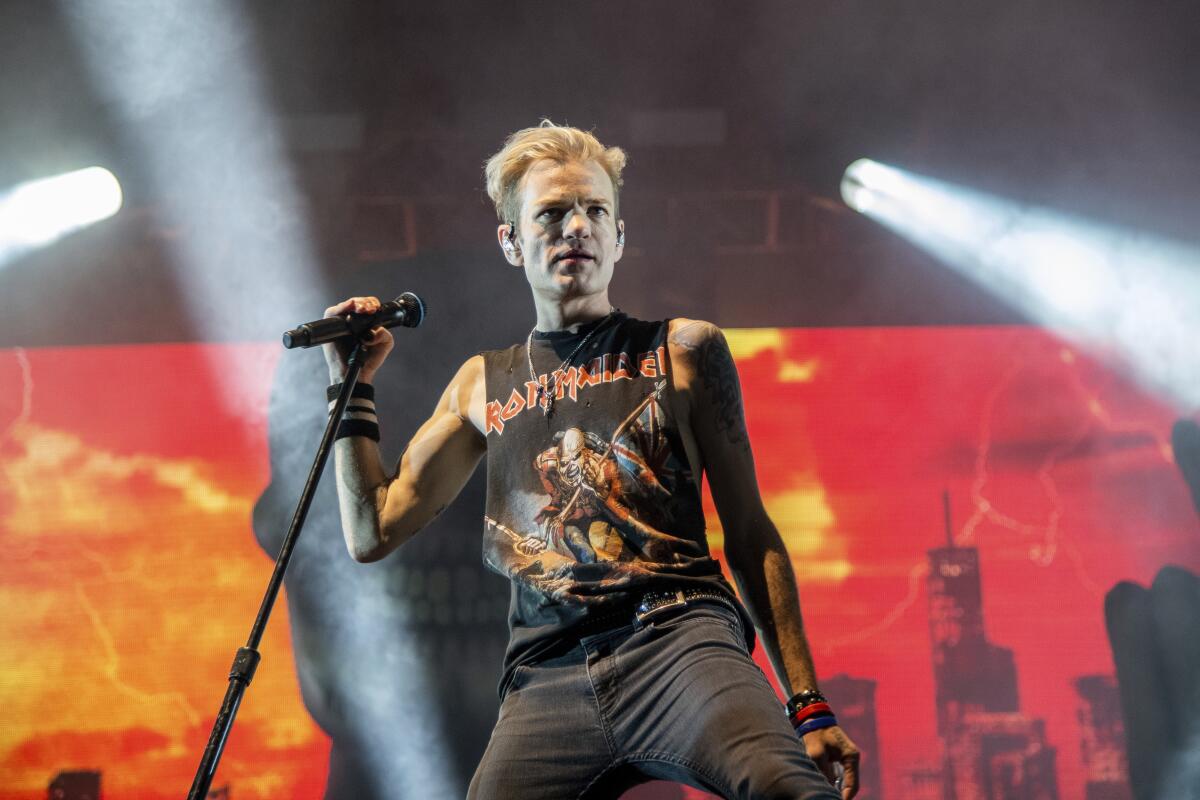 Deryck Whibley holds a microphone and stand onstage in black and red shirt with gray pants