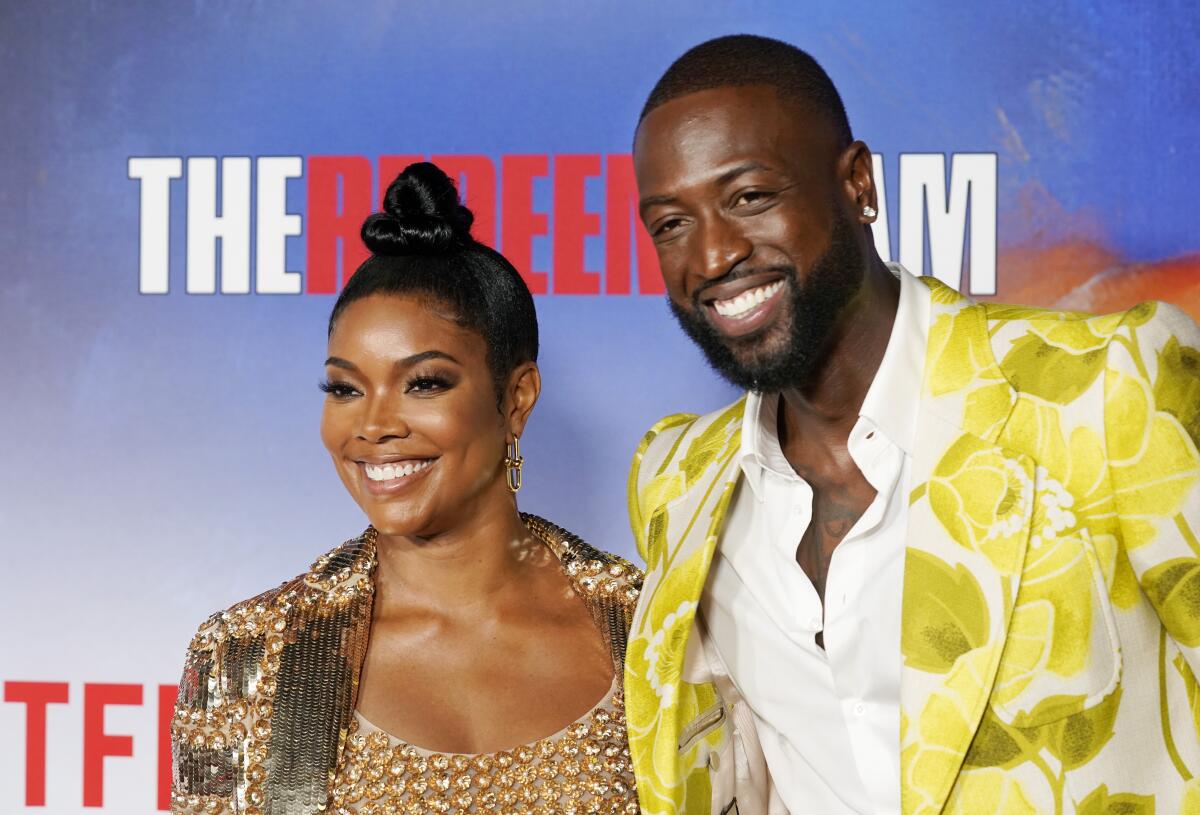 Gabrielle Union, in a bronze blazer and top, smiles for photos with Dwyane Wade, in a blazer with yellow and green flowers