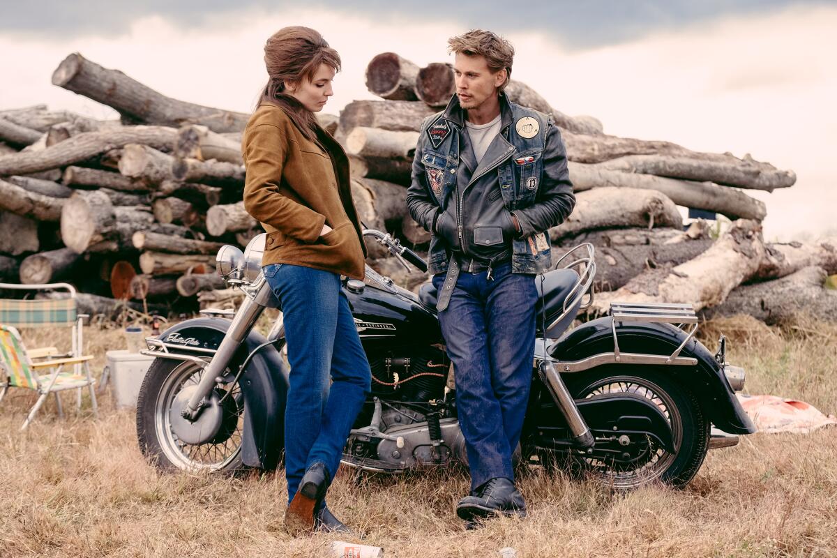 A woman flirts with a man leaning against a motorcycle.