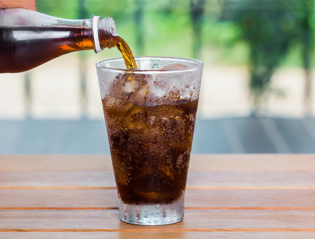 Cola drink is poured into a glass with ice.