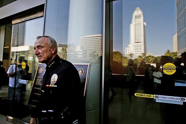 Los Angeles Police Chief William J. Bratton stands in front of the new police headquarters building, with City Hall reflected in the glass behind him.