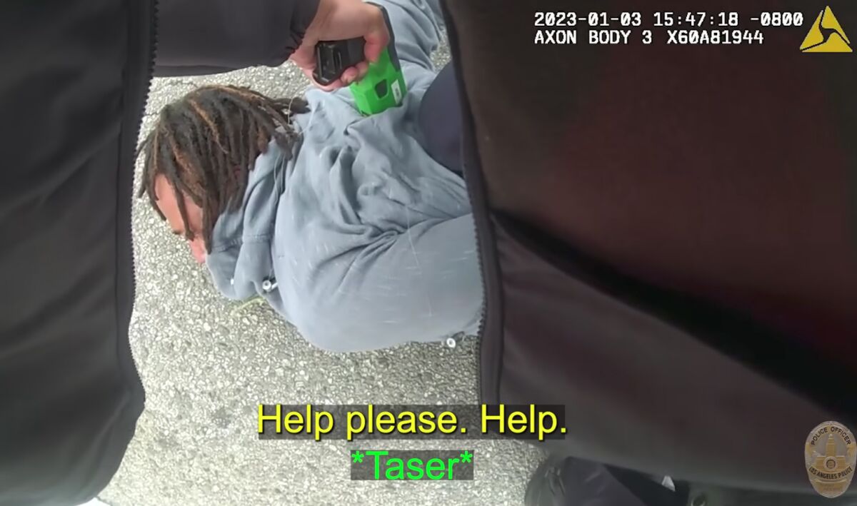 Video footage of a man being restrained on the ground by a police officer while another officer points a Taser at him. 