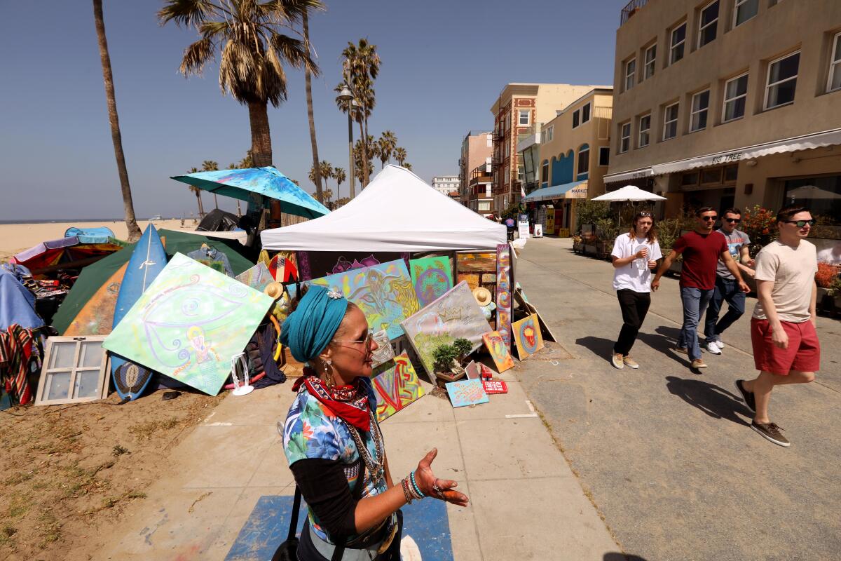 A woman stands by a tent with artwork as people walk by