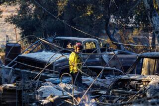 LAKE ELSINORE, CA - SEPTEMBER 11, 2024: A Riverside County firefighter checks for hotspots among burned cars and a destroyed home off Ortega Highway on September 11, 2024 in Lake Elsinore, California. (Gina Ferazzi / Los Angeles Times)