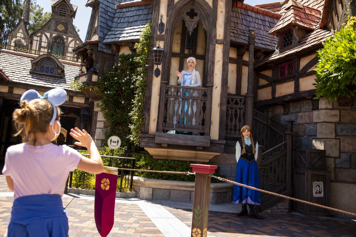 A young visitor waves at Elsa and Anna characters at Disneyland Resort on May 3, 2021. 