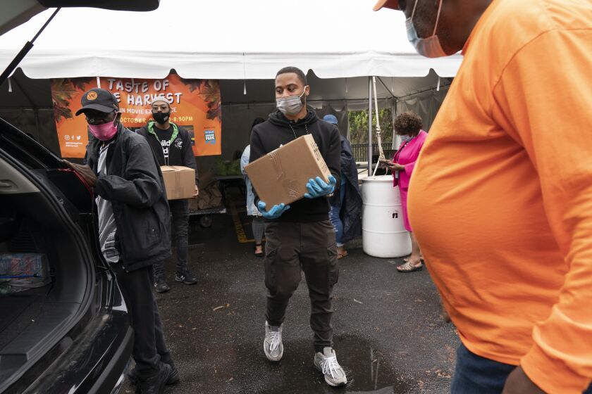Volunteer Markel Lucas, center, takes a box of food to a patron of the food bank's car, at the Town Hall Education Arts & Recreation Campus (THEARC), Wednesday, Oct. 6, 2021, in Washington. (AP Photo/Jacquelyn Martin)
