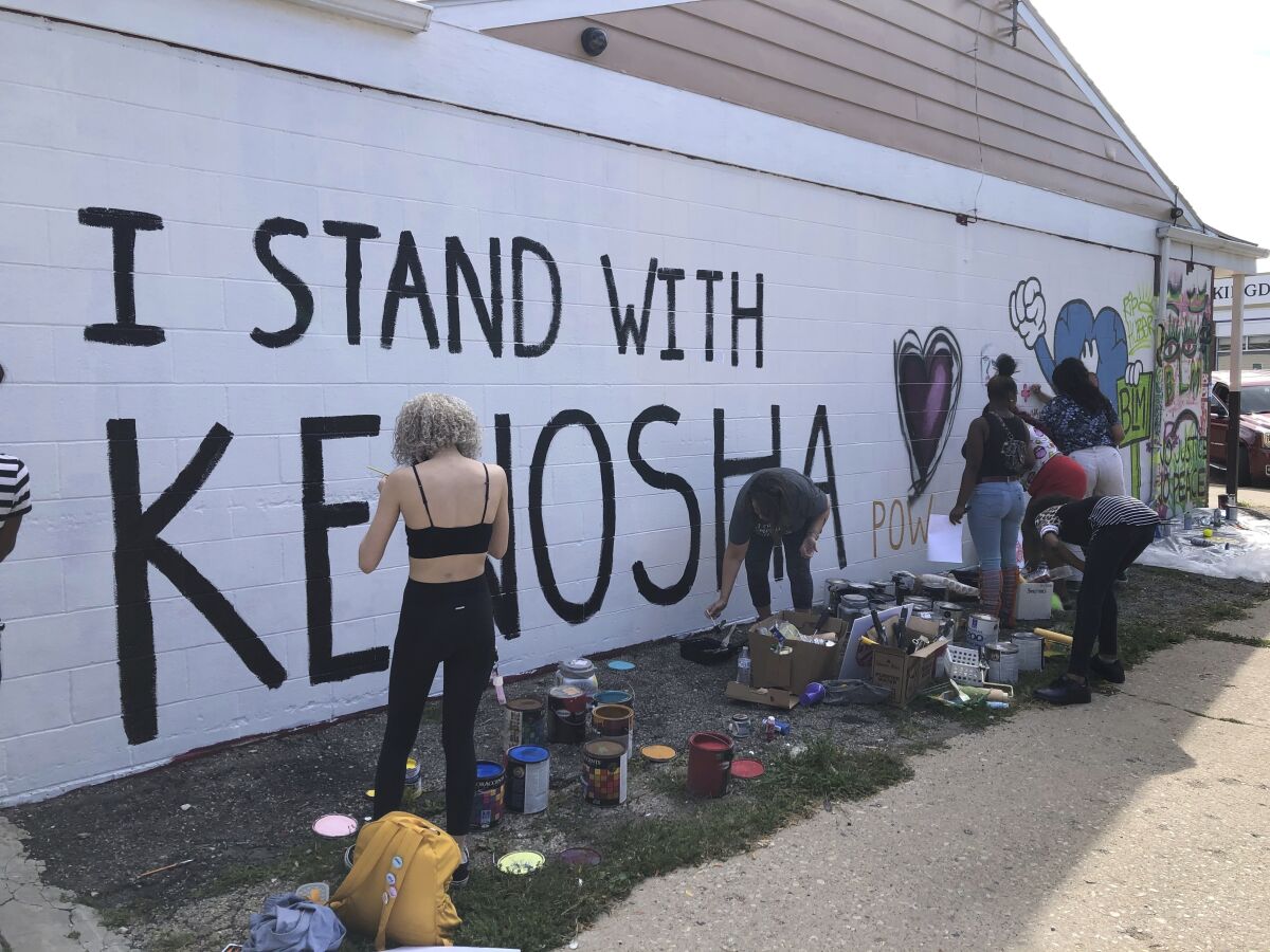 Volunteers paint murals on boarded-up businesses in Kenosha, Wis.