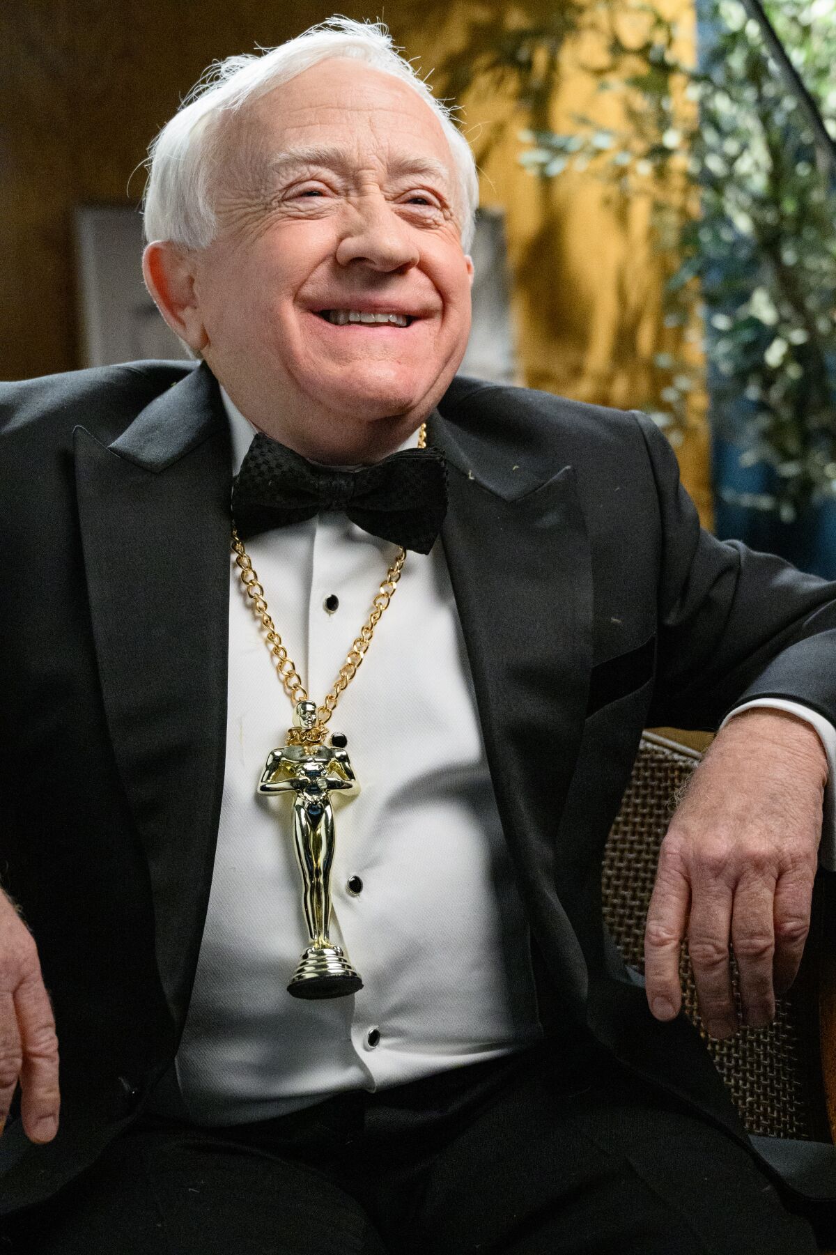 A man in a tuxedo wears a necklace with an Oscars statuette.