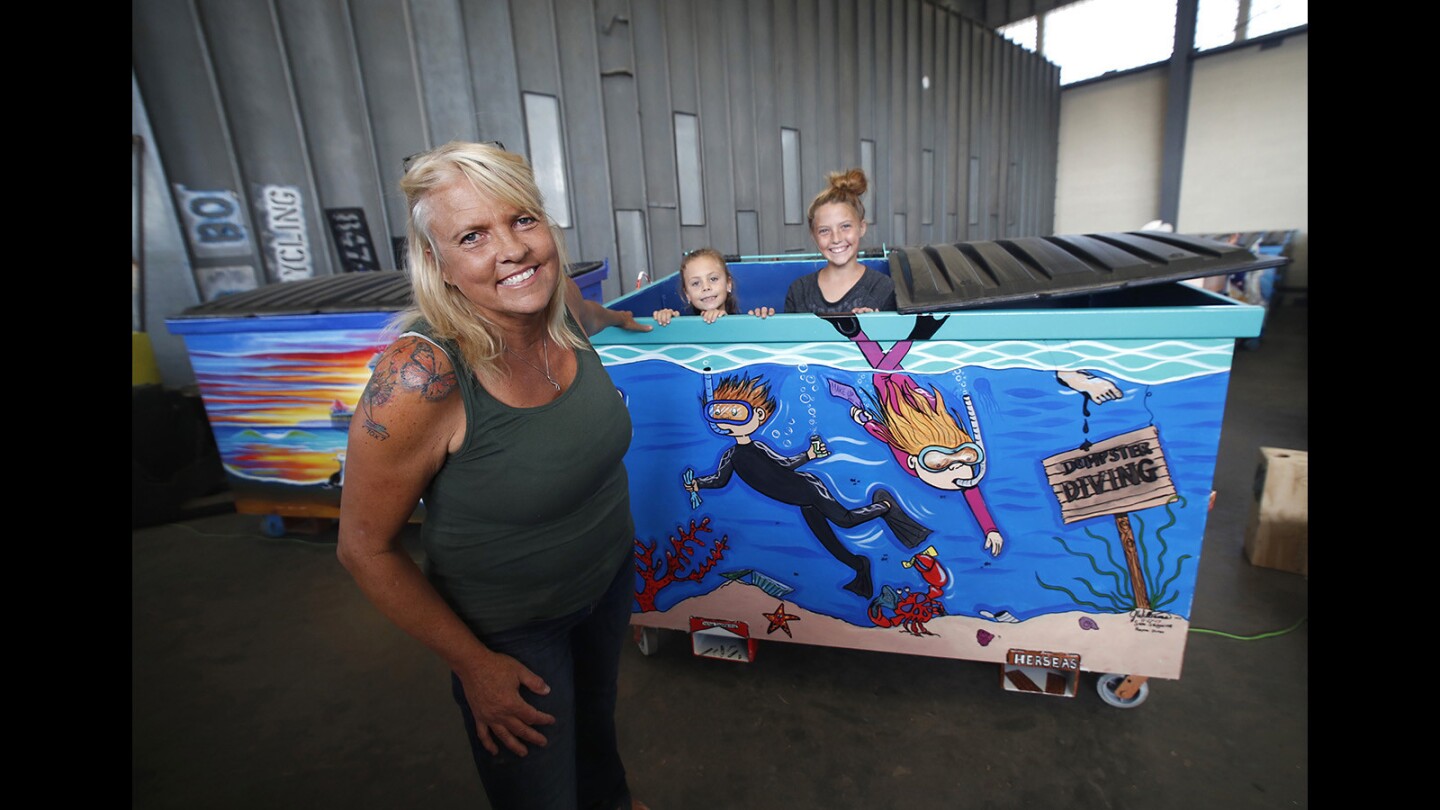 Artist Jody Williams, granddaughter Rayna Duran, 8, and daughter Samantha Seguine, 11, stand next to Williams' trash container named "Dumpster Diving," painted for the Huntington Beach Public Art Alliance's Dumpsters on Parade project.