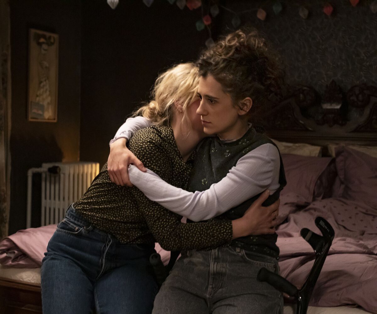 Two women hug while seated on a bed.