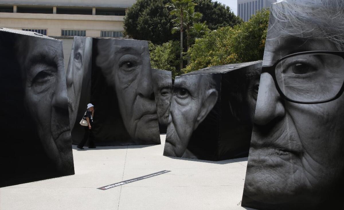 A woman walks through a portion of "iwitness," the first public art installation in Grand Park , featuring large-scale photographic sculptures bearing portraits of Armenian Genocide survivors and their stories.