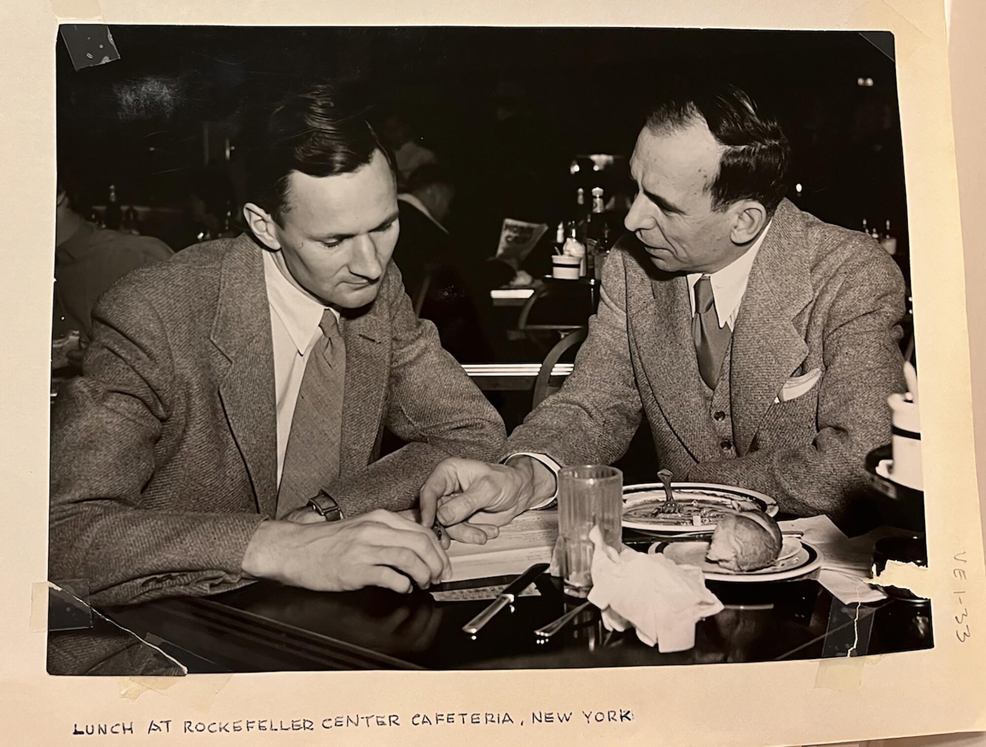     Two men in suits sitting at a table talking.